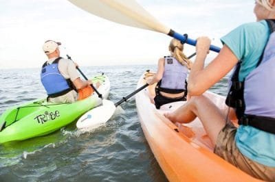 3 people cluster while paddling their sit on top kayaks in the ocean