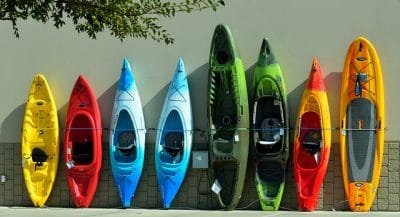 An assortment of short and tall kayaks standing on end against a wall