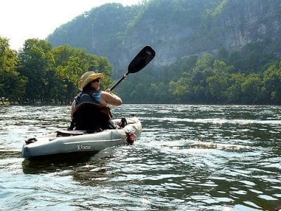 Tall woman in a cowboy hat paddles a big kayak in a lake near the mountains