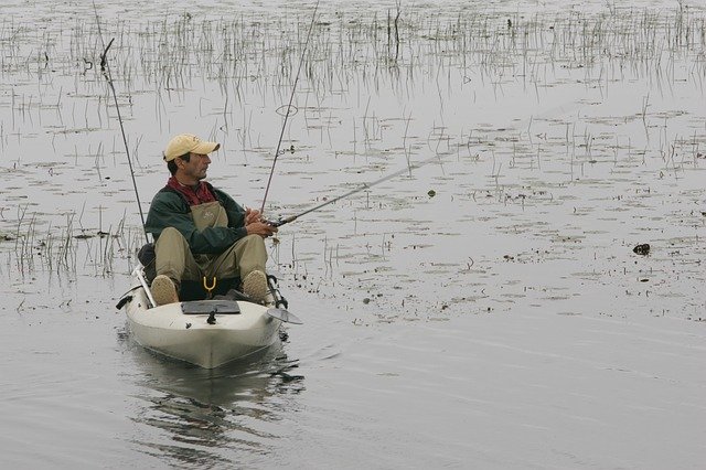 Man sits on his sit on top kayak fishing in a grassy marsh