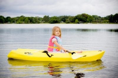 Little girl paddles a small, kid-sized kayak on a calm lake