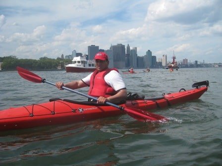 Man in a red hat, red vest, and red kayak paddles the busy waters near NYC