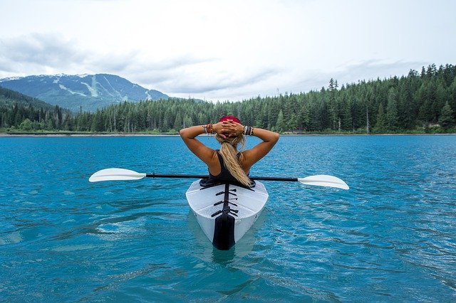 Young woman takes in the mountain scenery while she takes a break from paddling her foldable kayak