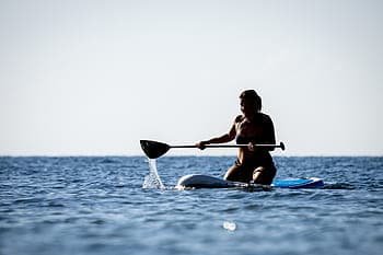 Woman in a bikini kneels while paddling an SUP in the ocean