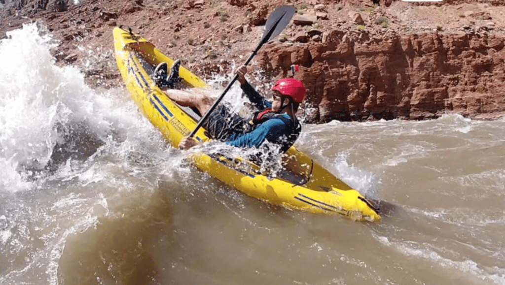 A whitewater kayaker powers through some rapids on an Advanced Elements Attack Pro whitewater inflatable kayak.