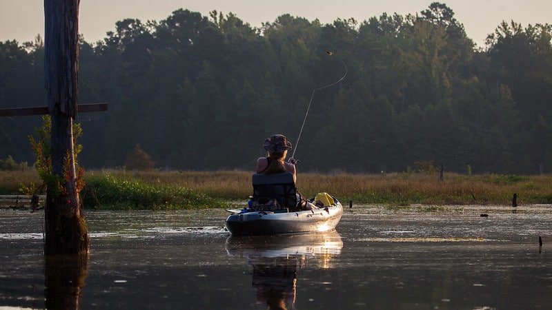 Sunrise photo of a kayak angler fishing in a shallow marsh