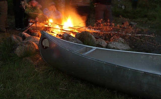 The stern of a canoe rests next to a warm and inviting evening campfire.