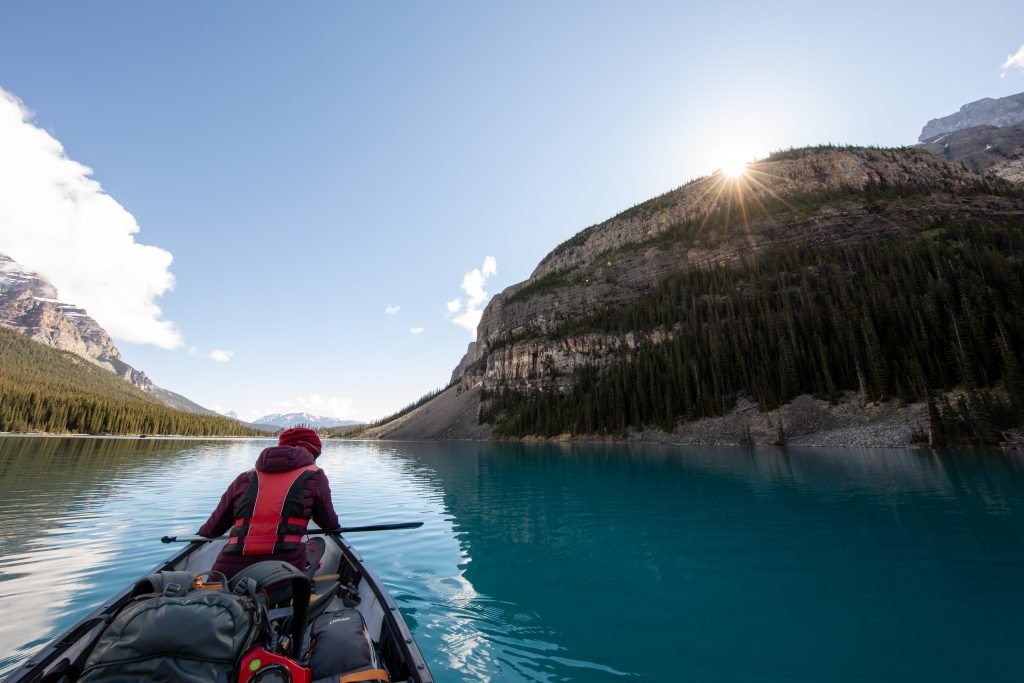 Front seat paddler in a canoe packed with camping gear drifts down a glacial waterway on a cold, sunny day